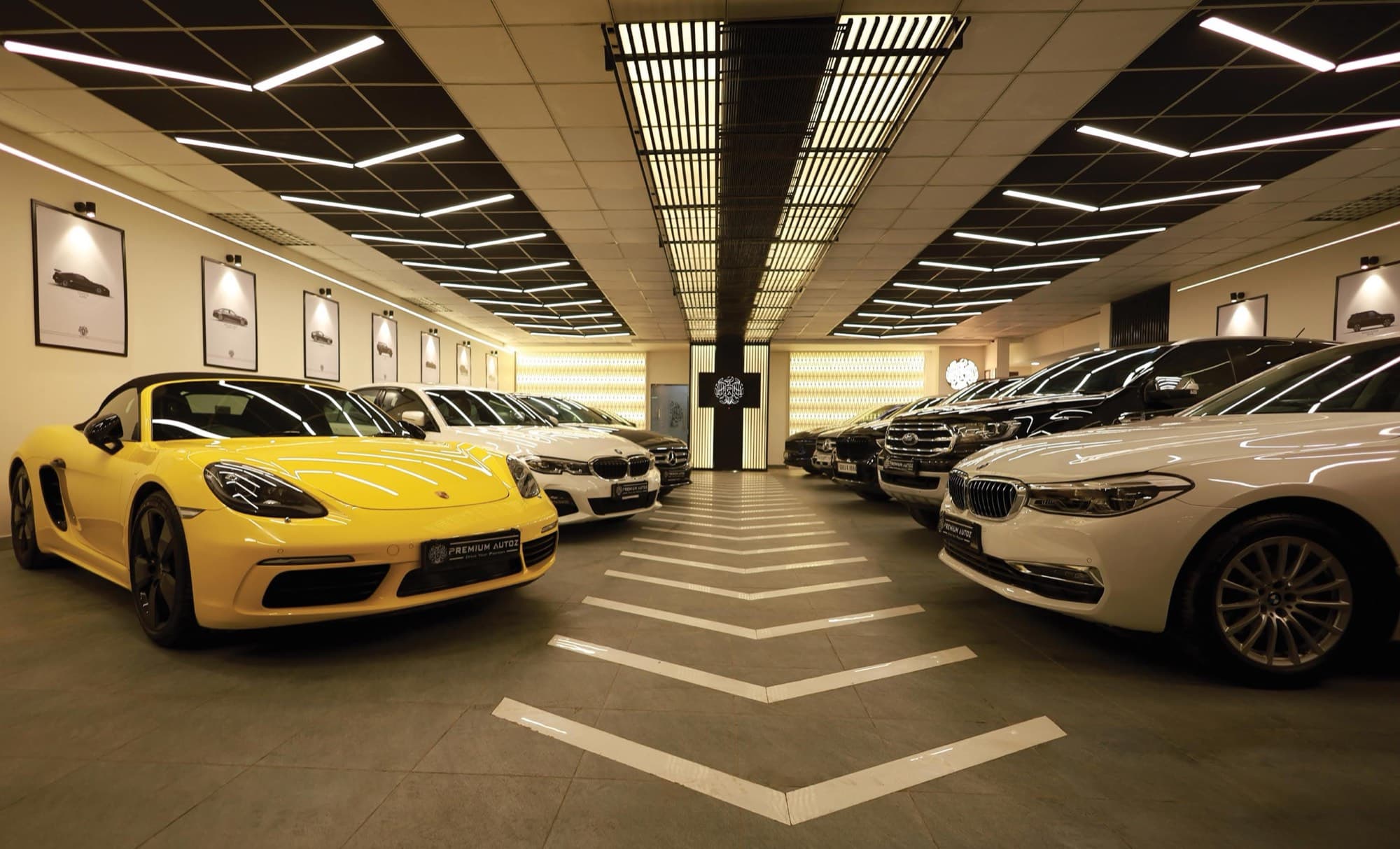 Showroom with a yellow sports car and saloons lined up beneath graphic linear lighting and a chevron floor