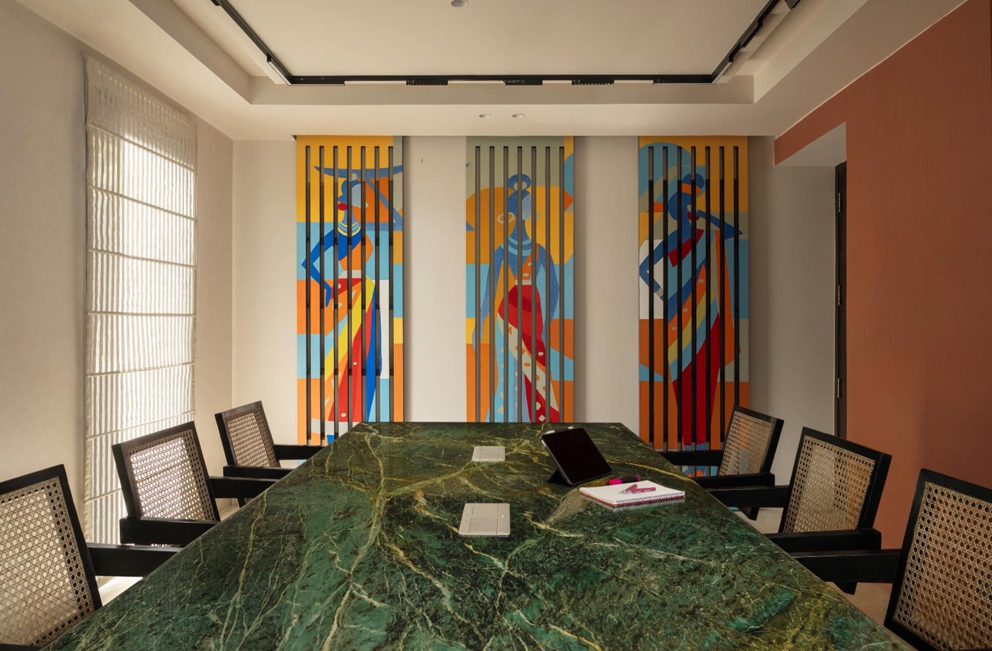 Conference room with a green marble table, cane chairs and painted tribal-art panels on a sliding screen